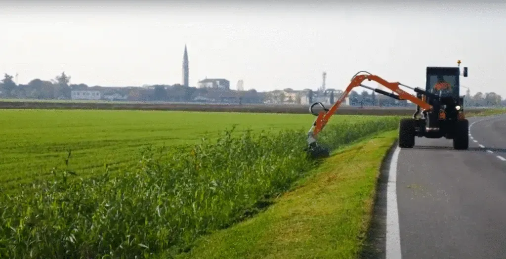 Tractor maintaining roadside grass in a scenic rural environment.