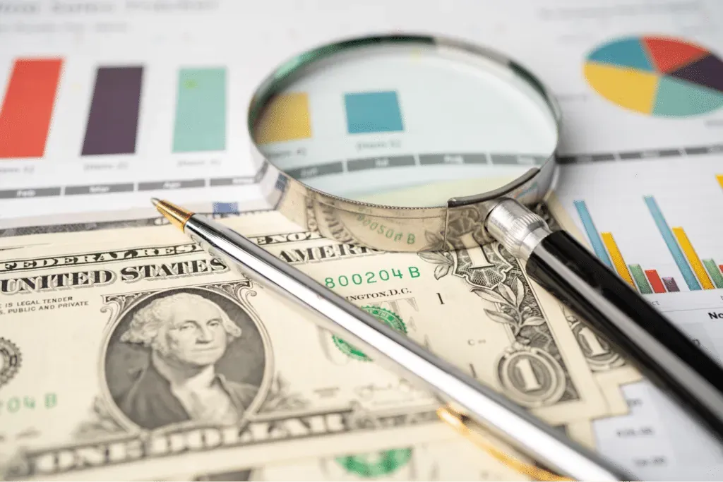 renting and purchasing equipment concept with a magnifying glass over currency and charts.