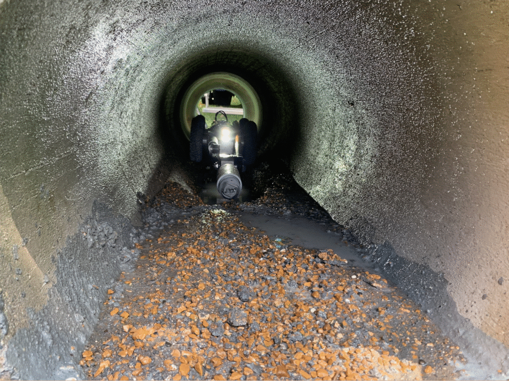 Worker inspecting drainage pipe for maintenance and clearing debris.