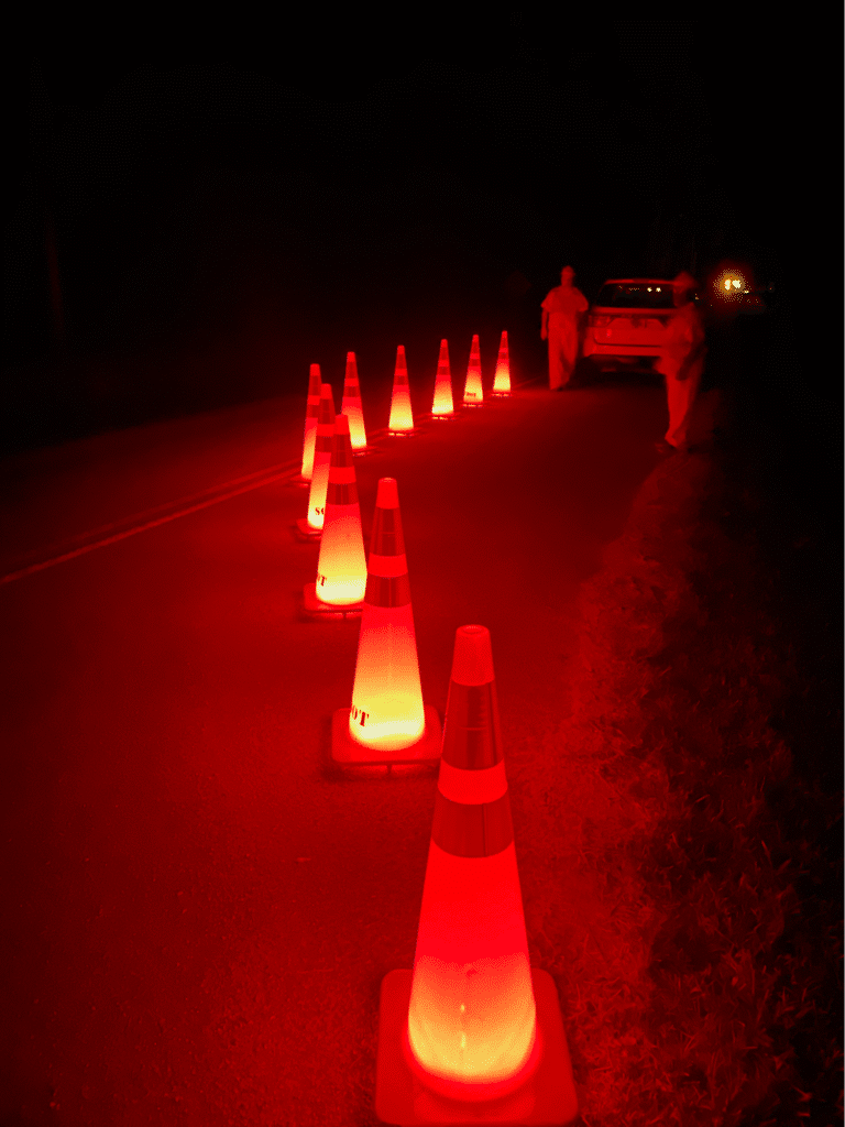 Red traffic cones light up a dark roadway for visibility and safety.