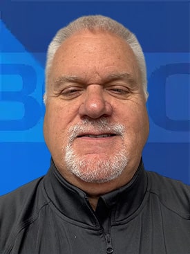Smiling man in a black jacket against a blue background, showcasing friendly demeanor.