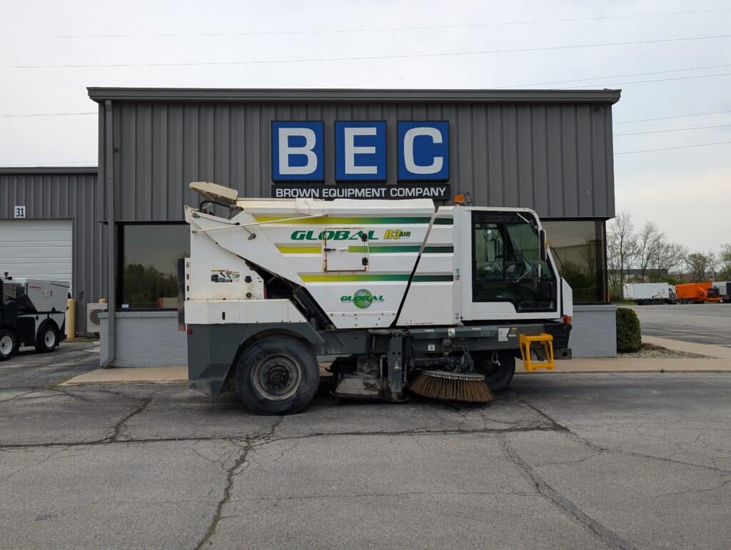 Brown equipment: Global street sweeper model JOHNSTON-3000-U in front of company building.