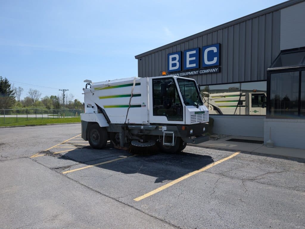 Street sweeper truck parked outside BEC equipment company for sale.