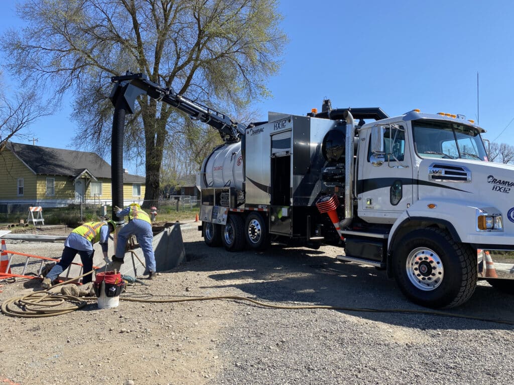 Construction workers operate heavy machinery at a job site under clear skies.
