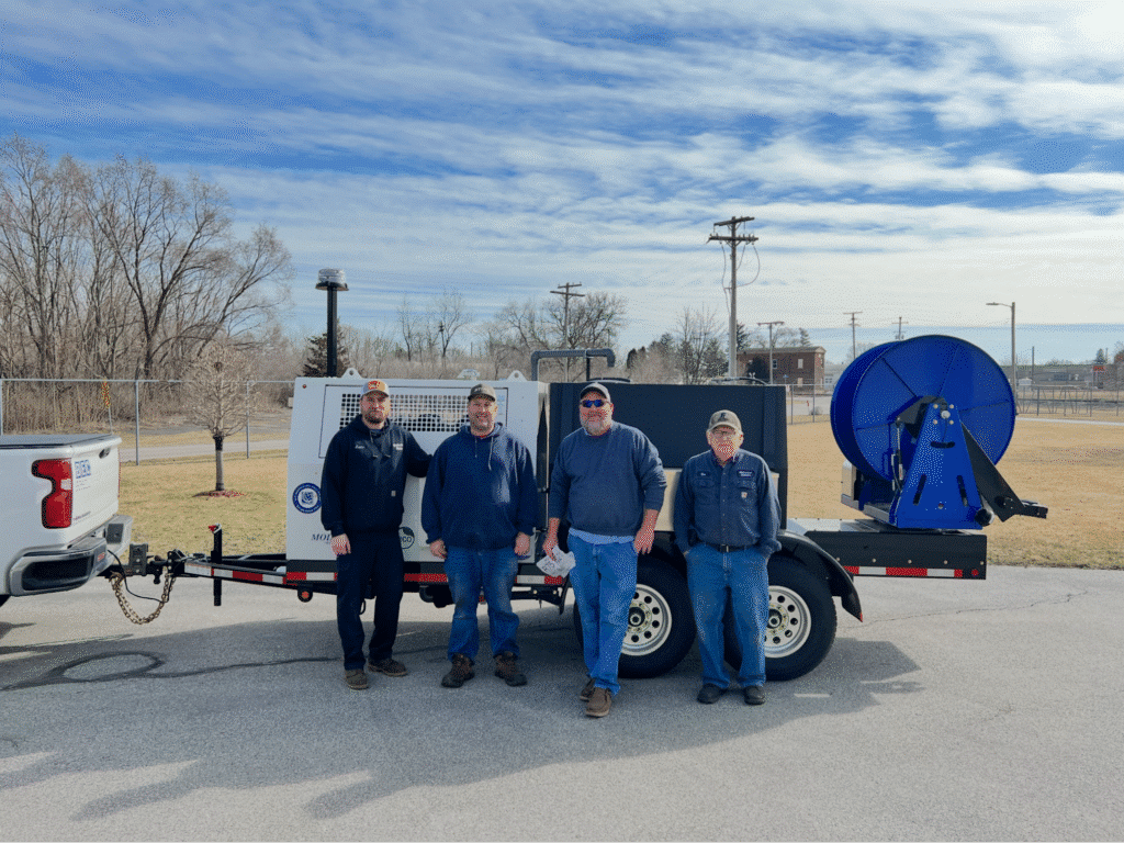 Team with trailer jetter machine in sunny landscape, ready for work.