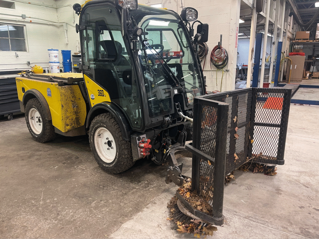 Compact utility vehicle clearing debris in a warehouse setting.