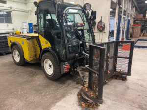 Compact utility vehicle clearing debris in a warehouse setting.
