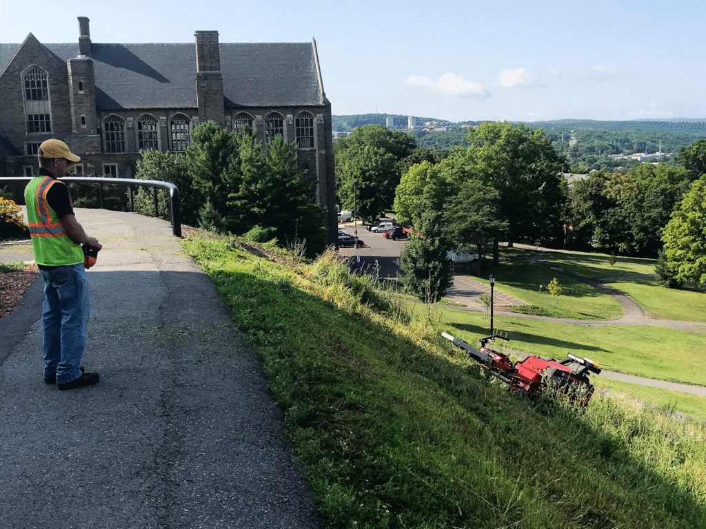 Professional landscape maintenance featuring a worker using machinery on a hillside.