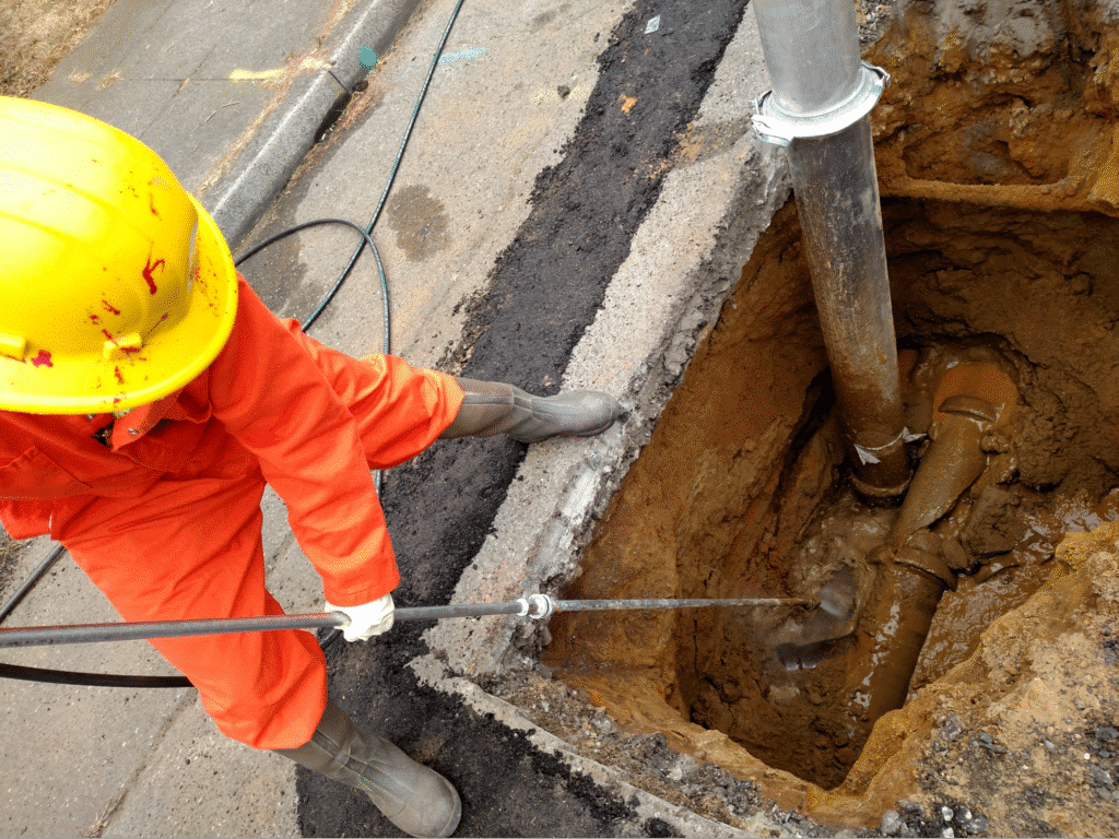 Worker clearing a clogged drain with high-pressure hydro excavation equipment in an underground system.