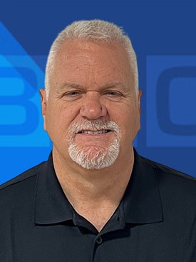 Professional headshot of a smiling man with a white beard against a blue background.