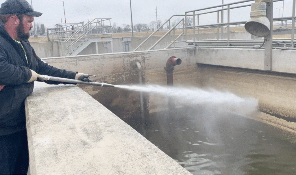 Worker using high-pressure water to clean water treatment facility tank.