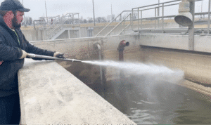 Worker using high-pressure water to clean water treatment facility tank.