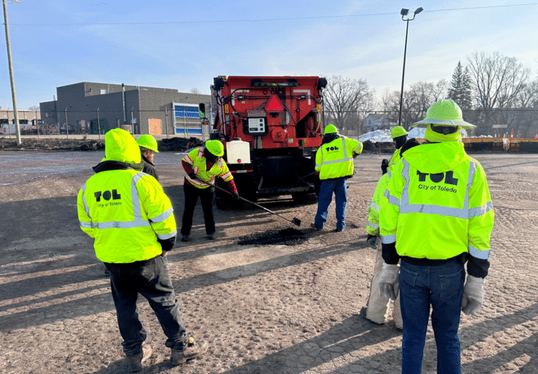 Workers in high-visibility jackets repairing a surface in an outdoor setting.