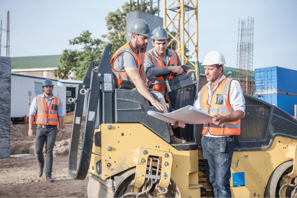 Construction team reviewing project plans with heavy machinery on-site.