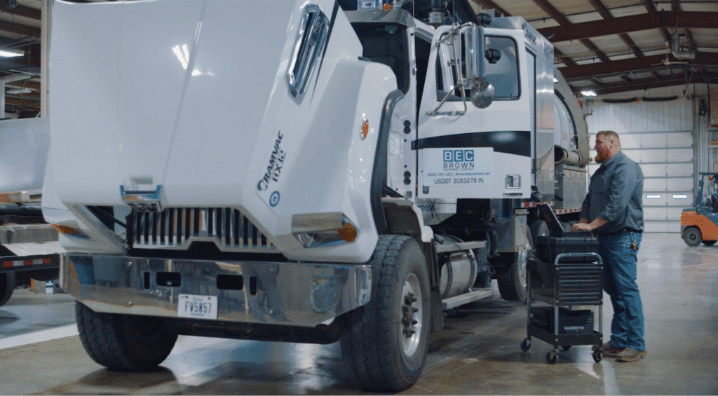 Mechanic performing maintenance on a heavy-duty garbage truck in a garage.