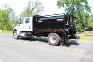 Black waste management truck driving on a rural road, highlighting efficient services.