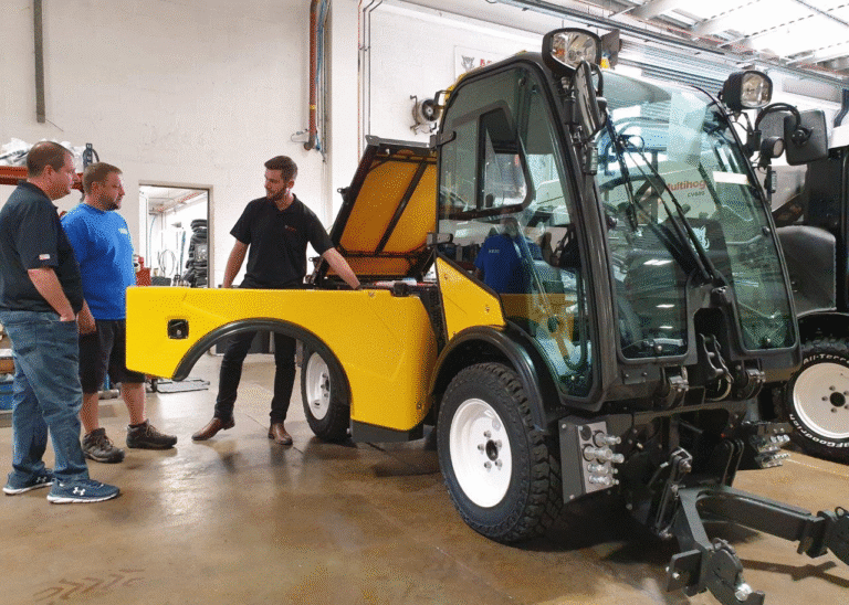Men collaborating on a yellow utility vehicle in a workshop environment.