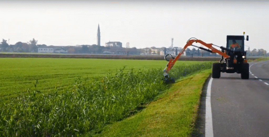 Tractor maintaining roadside grass in a scenic rural environment.