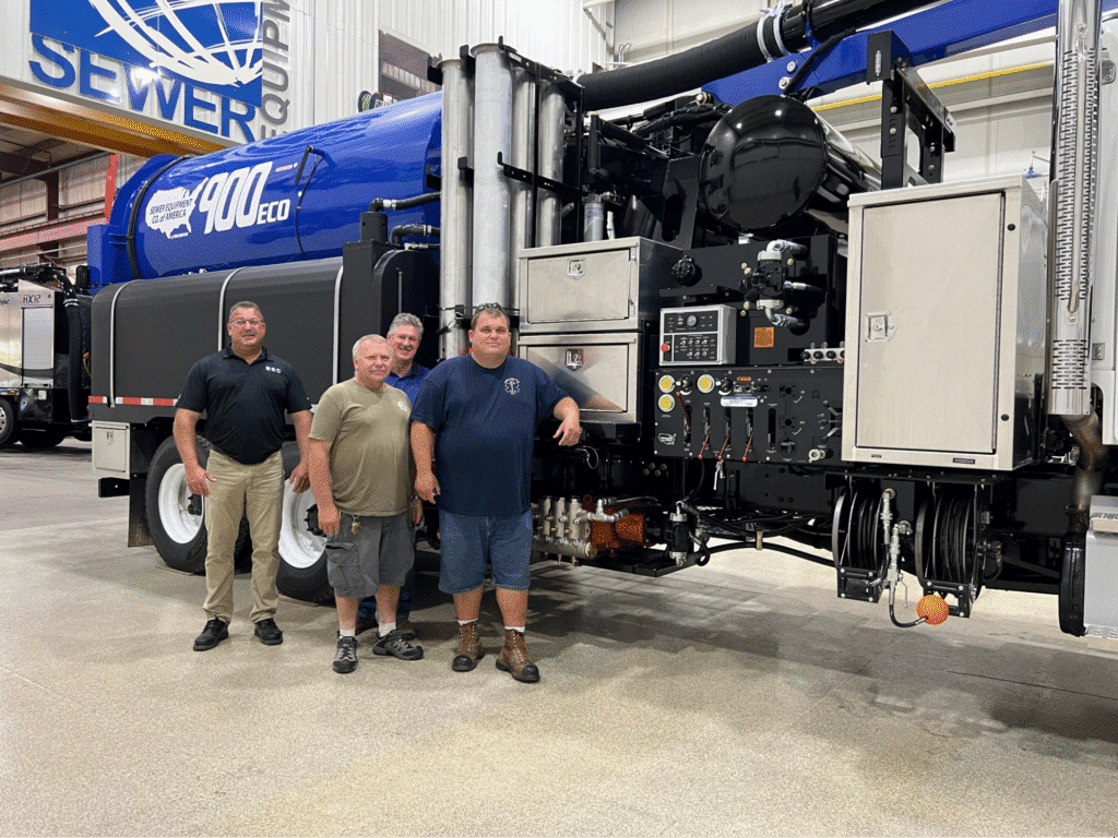 Three experts beside advanced vacuum truck in a sewer maintenance facility.