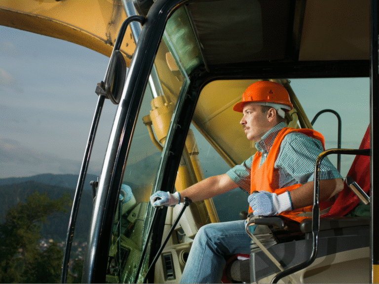 Heavy machinery operator focused on work in a safety helmet and vest.