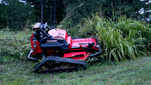 Remote-controlled mower clearing tall grass in a landscaped area.