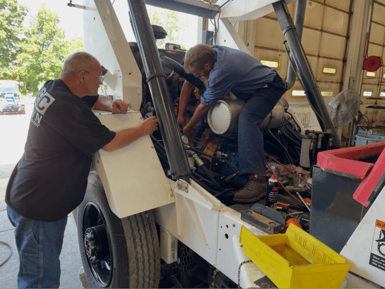 Two mechanics repairing a truck engine inside a garage.