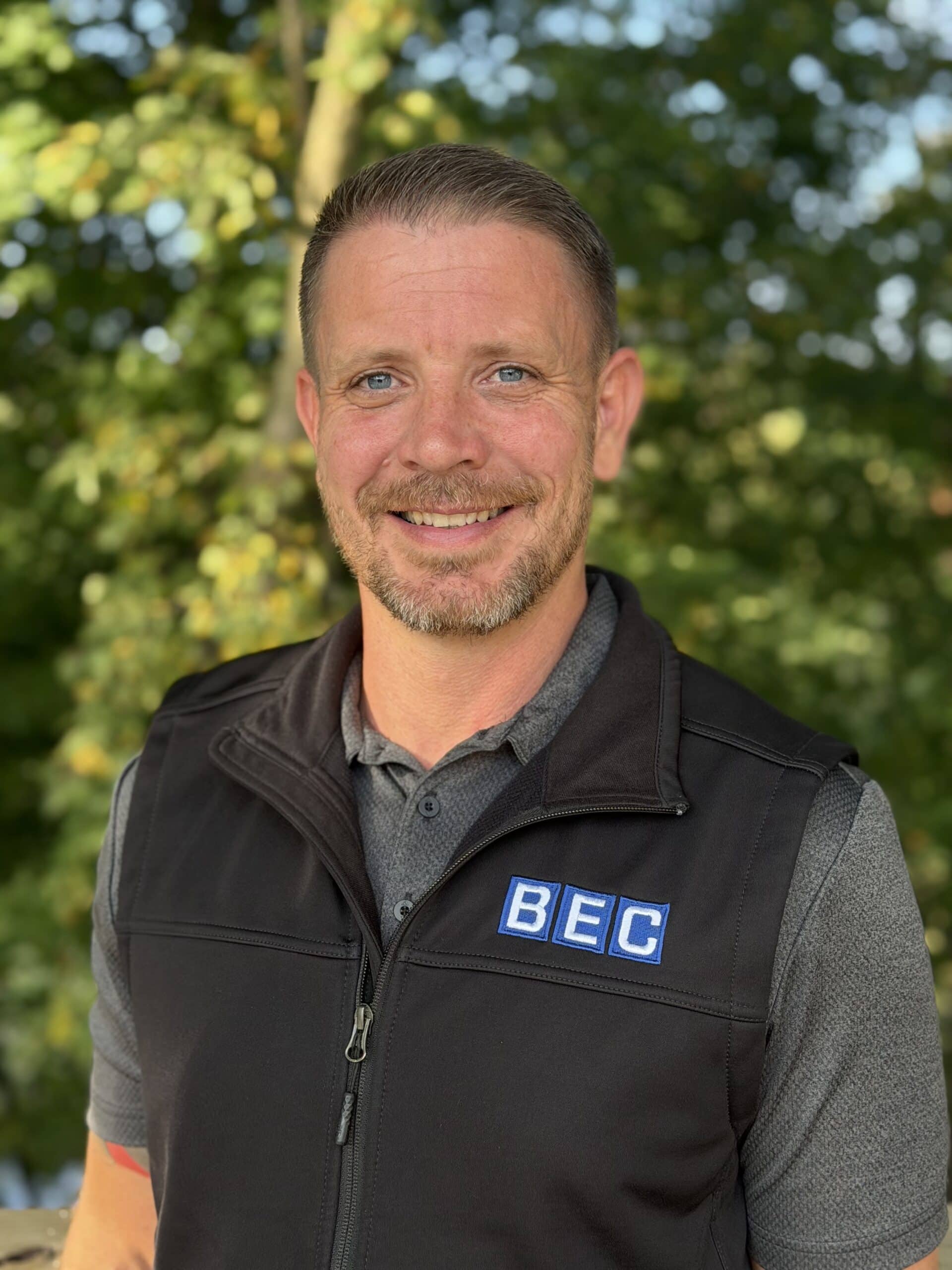 BEC team member smiling outdoors, showcasing professionalism and approachability in a nature setting.
