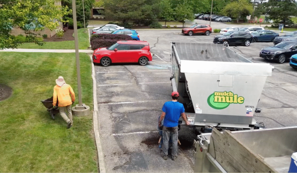 Landscapers working on lawn maintenance with a Mulch Mule trailer in a parking lot.