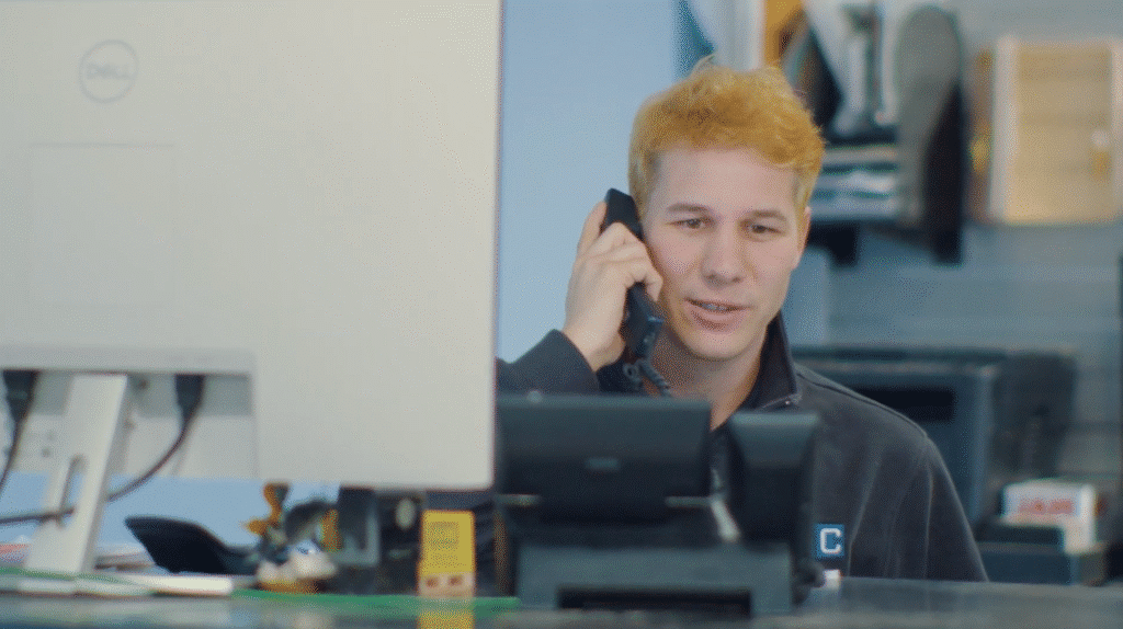 Customer service representative with Brown Equipment Company, a landscaping equipment dealer, helping clients on the phone at a modern office.