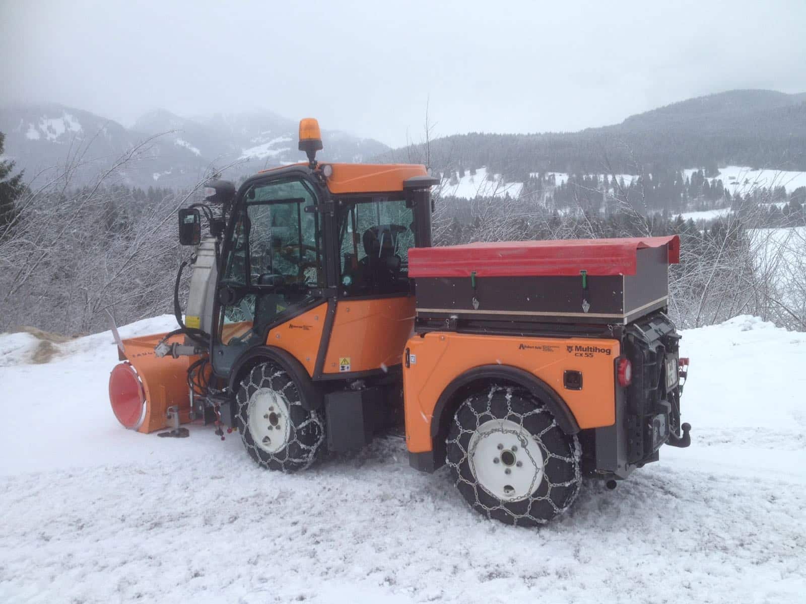 Orange multihog vehicle clearing snow in winter landscape.