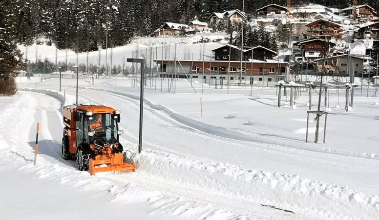 Snow plow clearing a snowy path in a winter landscape with cozy cabins.