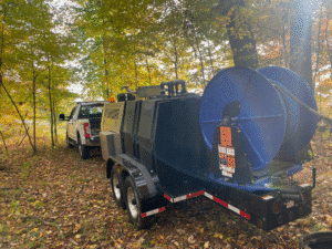 Trailer mounted with blue reel in wooded area, ready for outdoor equipment use.
