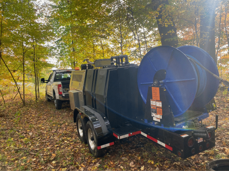 Trailer mounted with blue reel in wooded area, ready for outdoor equipment use.