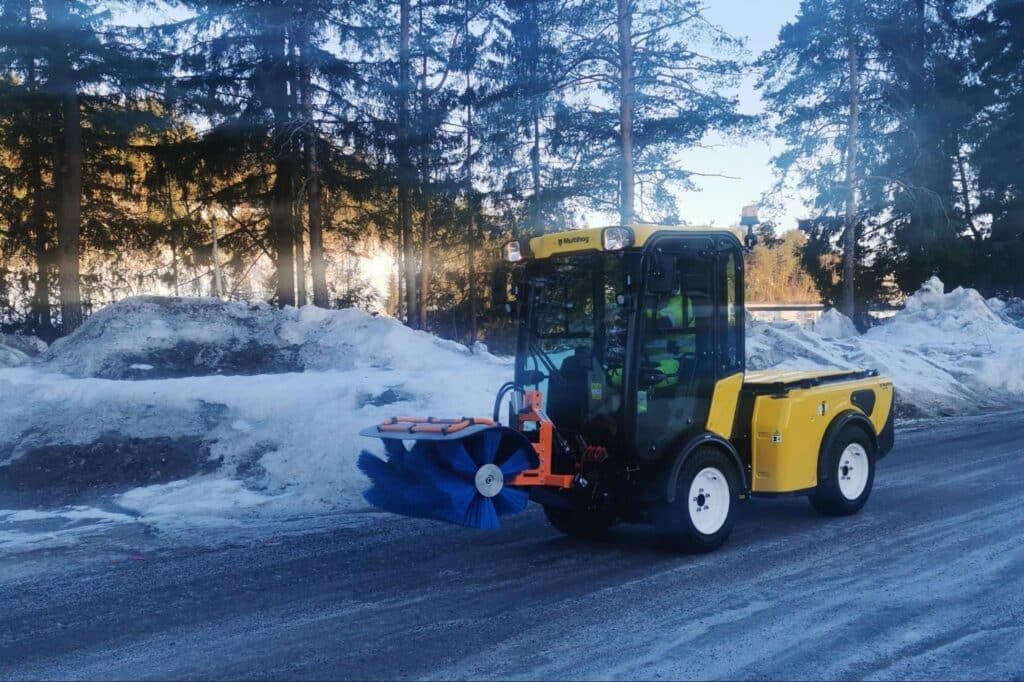 Snow plow clearing a winter road with snow piles in the background.