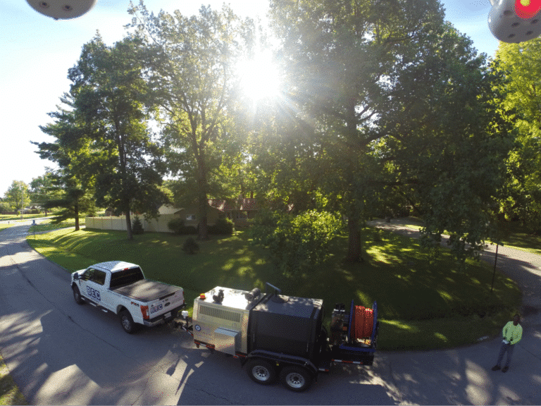 Maintenance equipment parked under a large tree in a residential area.