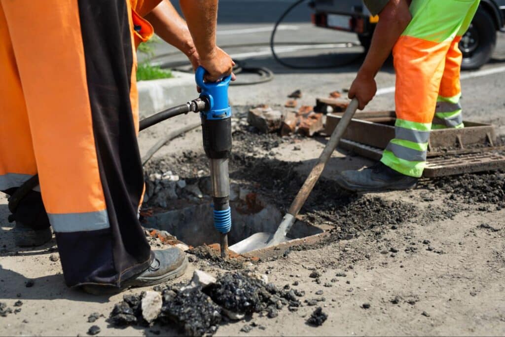 Construction workers repairing a road using a jackhammer and shovels.