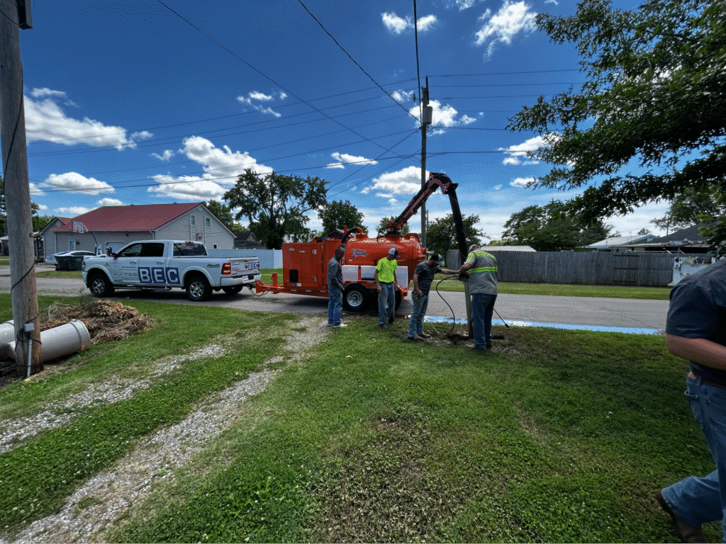 Workers operating performing narrow trench excavation for utility maintenance on a bright, sunny day.