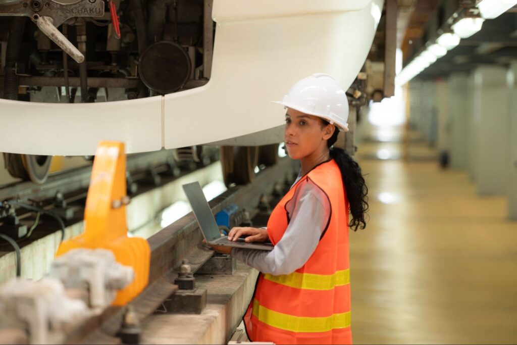A female engineer using a laptop in a train maintenance facility.