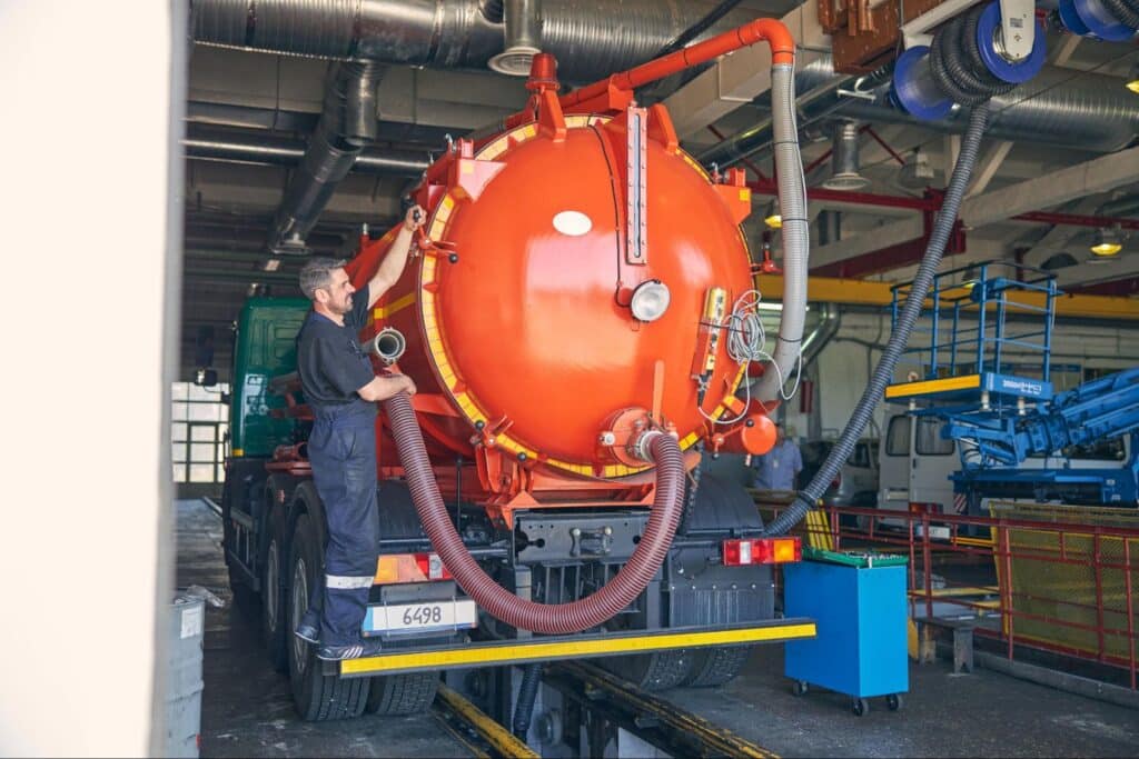Vacuum truck operator servicing sewer jet trucks in an industrial facility.