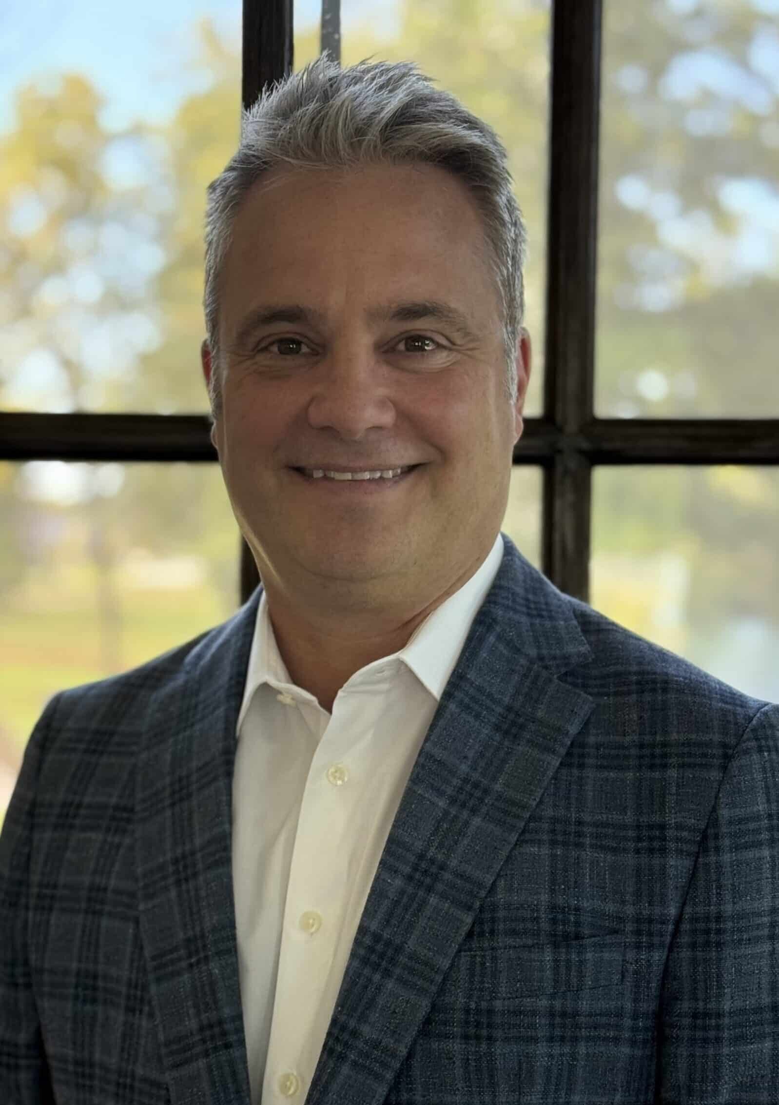 Confident businessman smiling in a professional suit near a window.