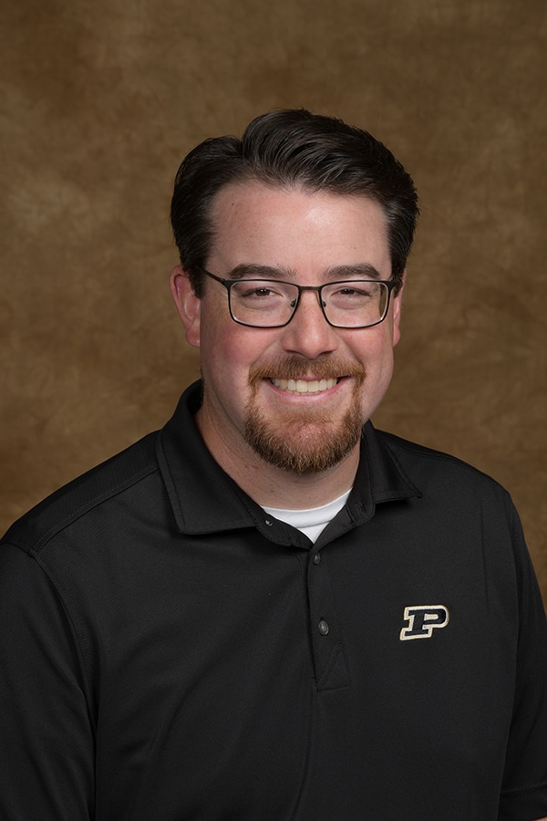 Smiling man in a black shirt, showcasing a friendly portrait on a textured background.