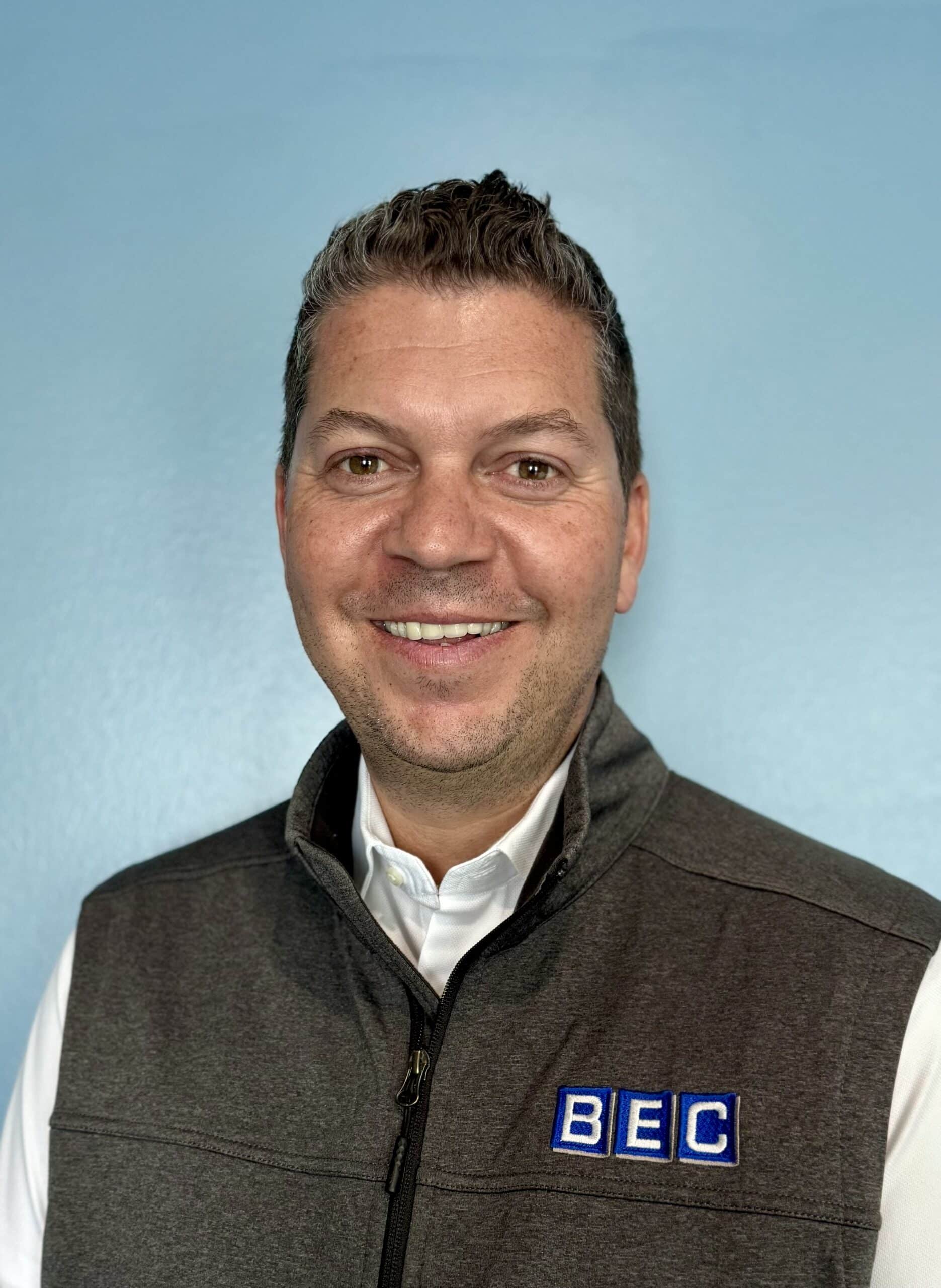 Smiling man in a vest with BEC logo against a blue background.