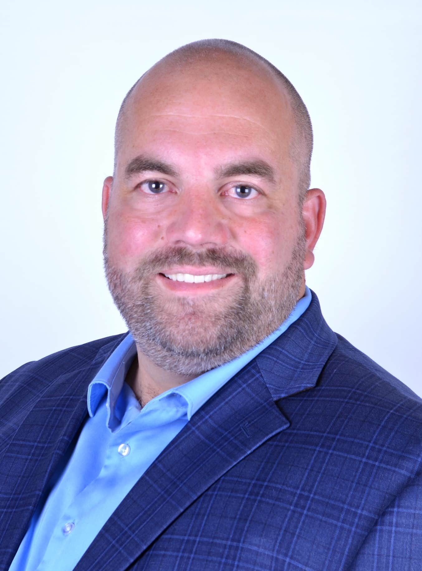 Professional businessman in a blue suit smiling confidently for a business profile photo.