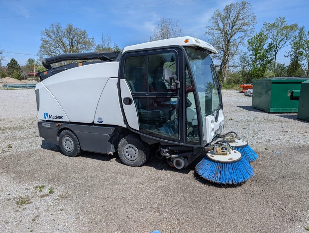 Compact street sweeper vehicle on gravel, ideal for efficient urban cleaning.