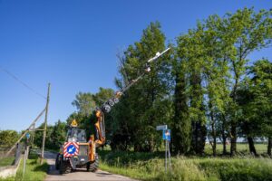 Utility vehicle working on power lines surrounded by trees on a sunny day.