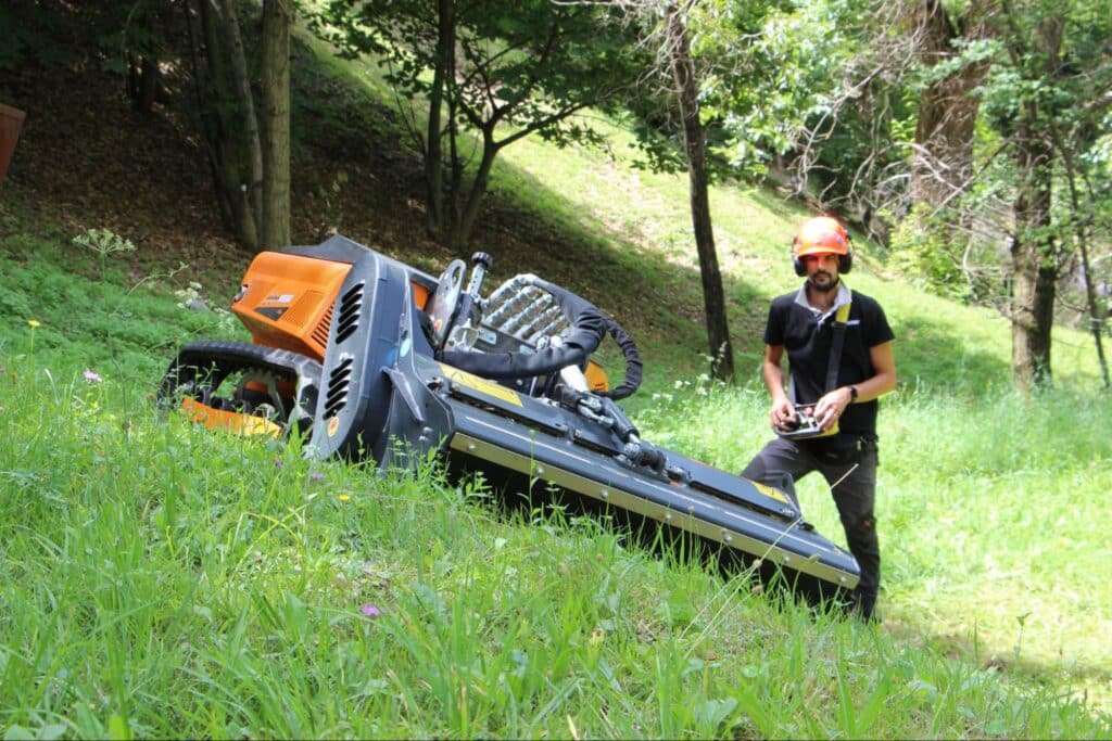 Operator using a powerful remote control mower on a hillside for effective land maintenance.