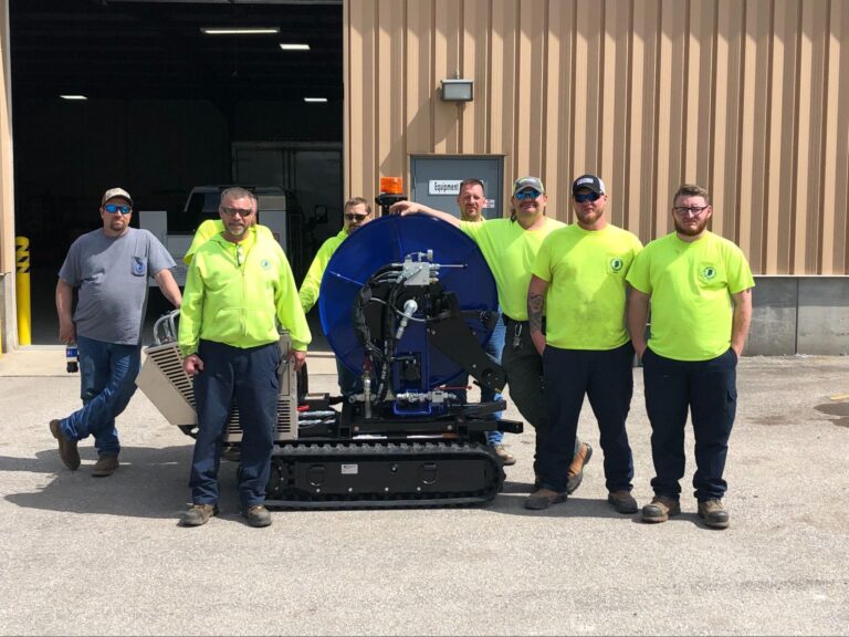 Team of workers in bright safety shirts posing with equipment outside a facility.