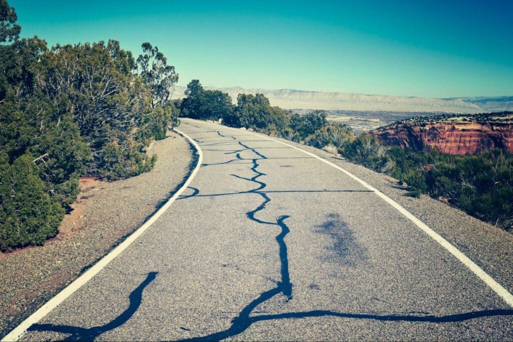 Cracked road winding through lush greenery in a picturesque rural setting.