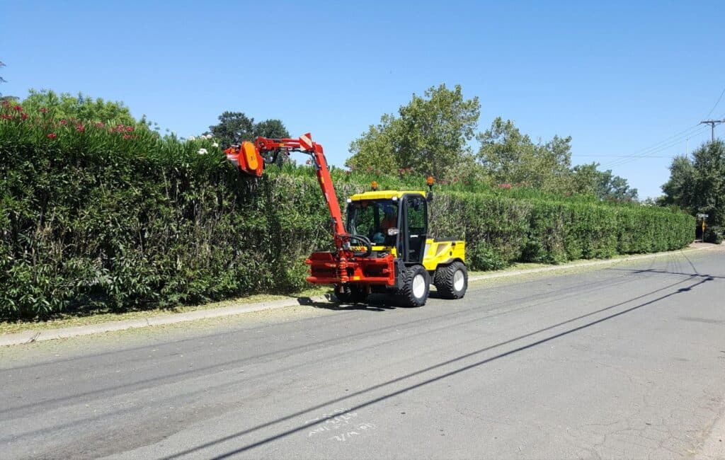 Efficient hedge trimming equipment working on a sunny street for landscape care.