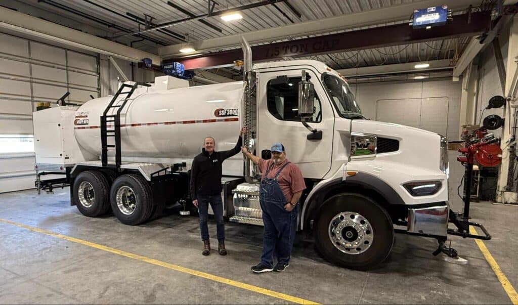 Two workers beside a modern fuel delivery truck in a garage.